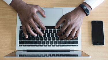 Picture of a person's hands typing on a laptop with a mobile phone on the desk.