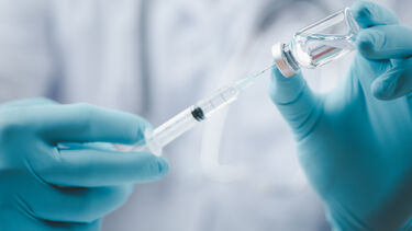 Gloved hands holding a syringe and small bottle of liquid
