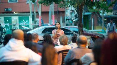 a speaker with a microphone, in front of a seated audience 