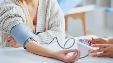 A woman in a white cardigan wearing a blood pressure cuff
