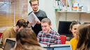  seminar class with students around their laptops and a teacher holing papers